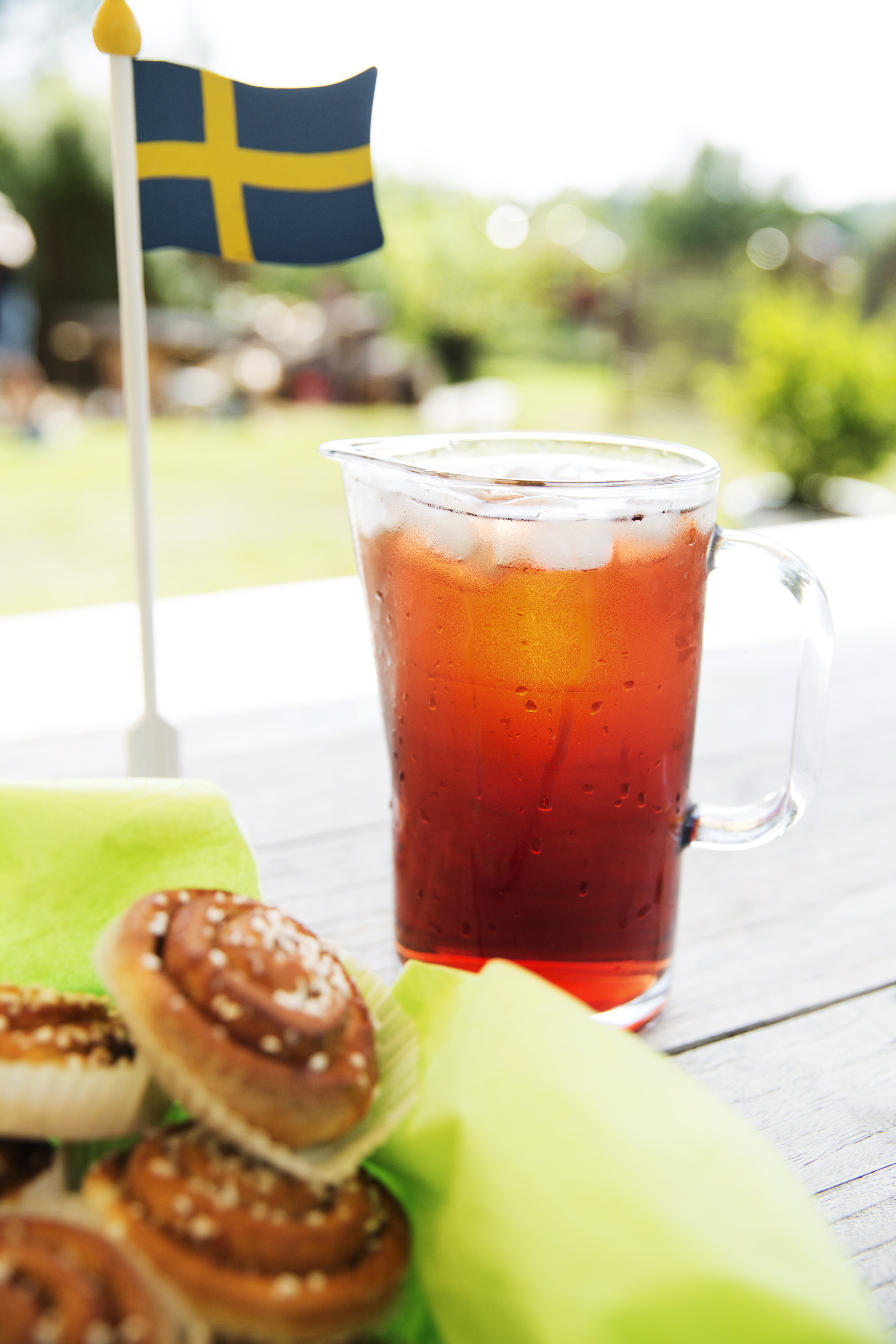 En kanna saft, en korg med bullar och en liten flaggstång i trä står på ett bord.