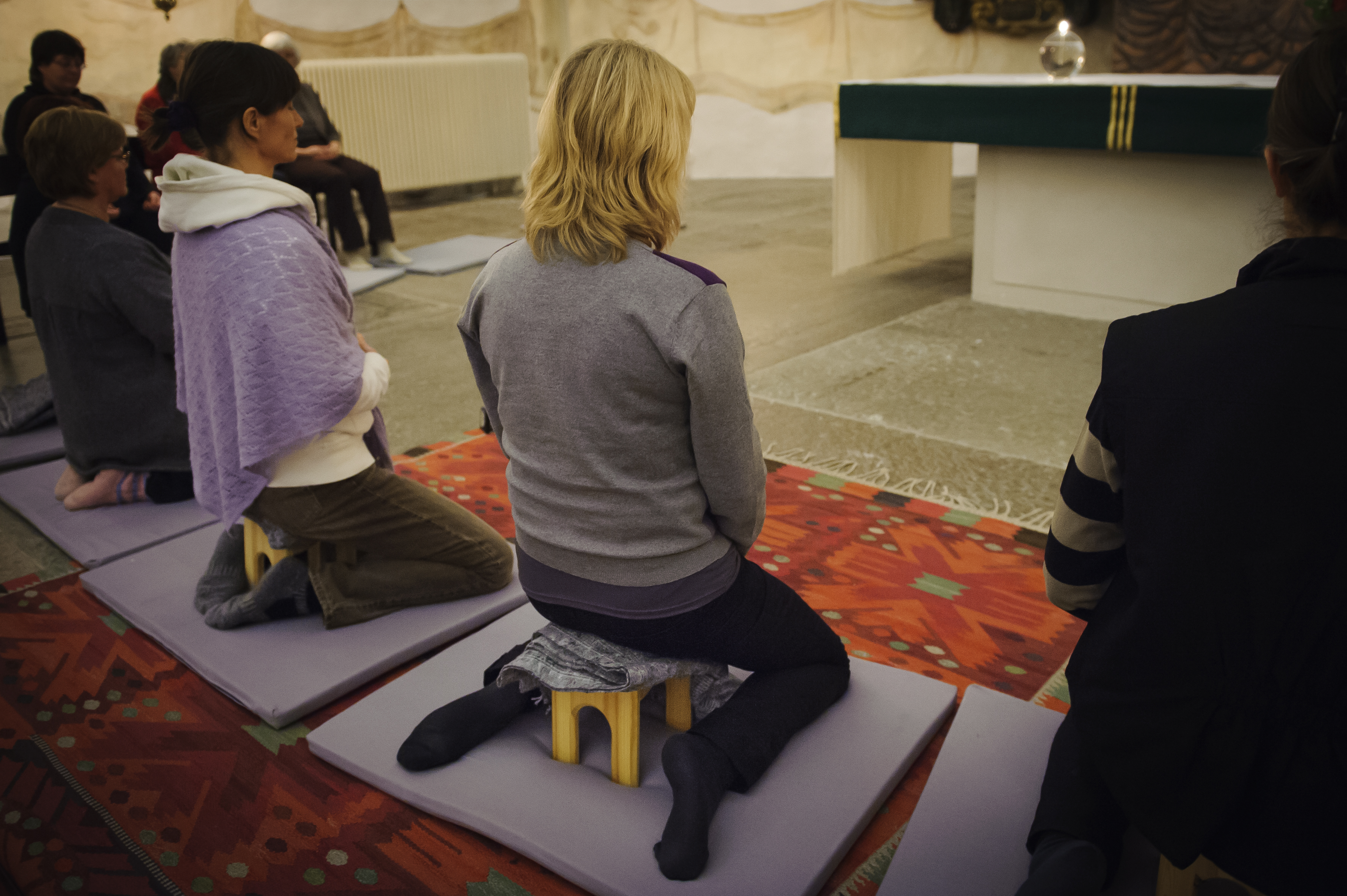 En grupp människor sitter på rad på små pallar framför ett altare.