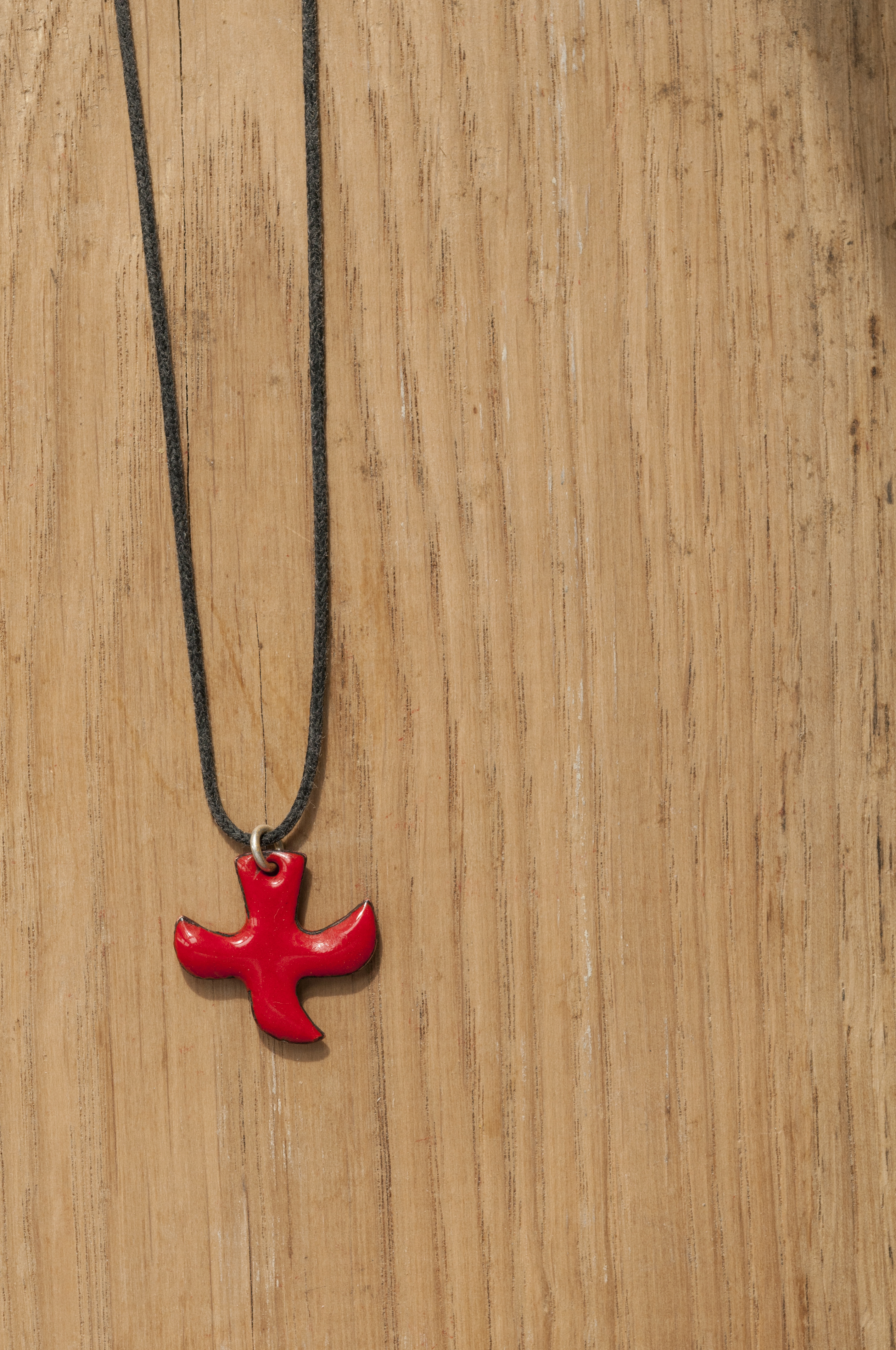 Ett halsband med ett rött Taizékors mot träbakgrund.