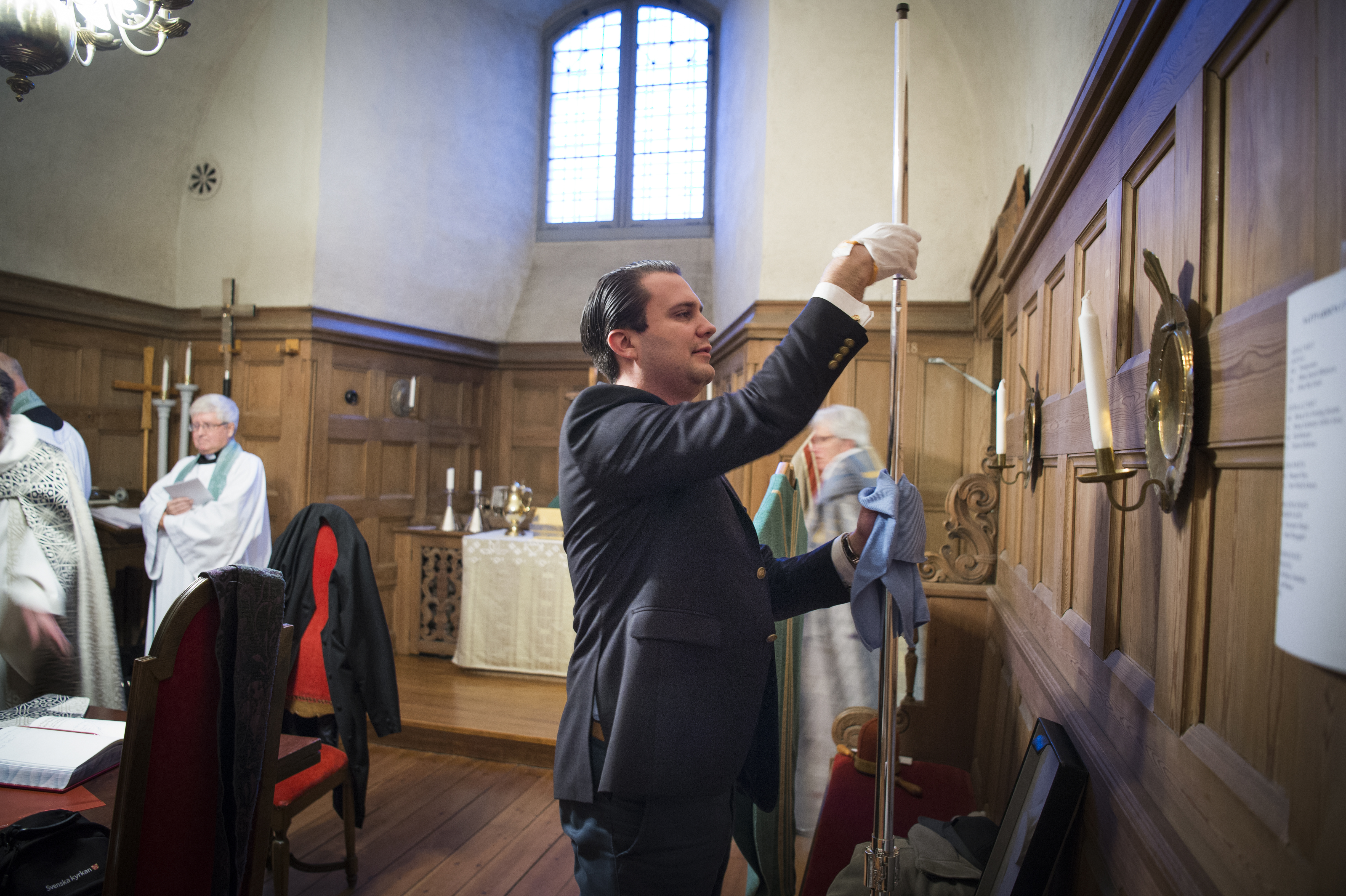 En kyrkvaktmästare putsar en biskopsstav i sakristian.