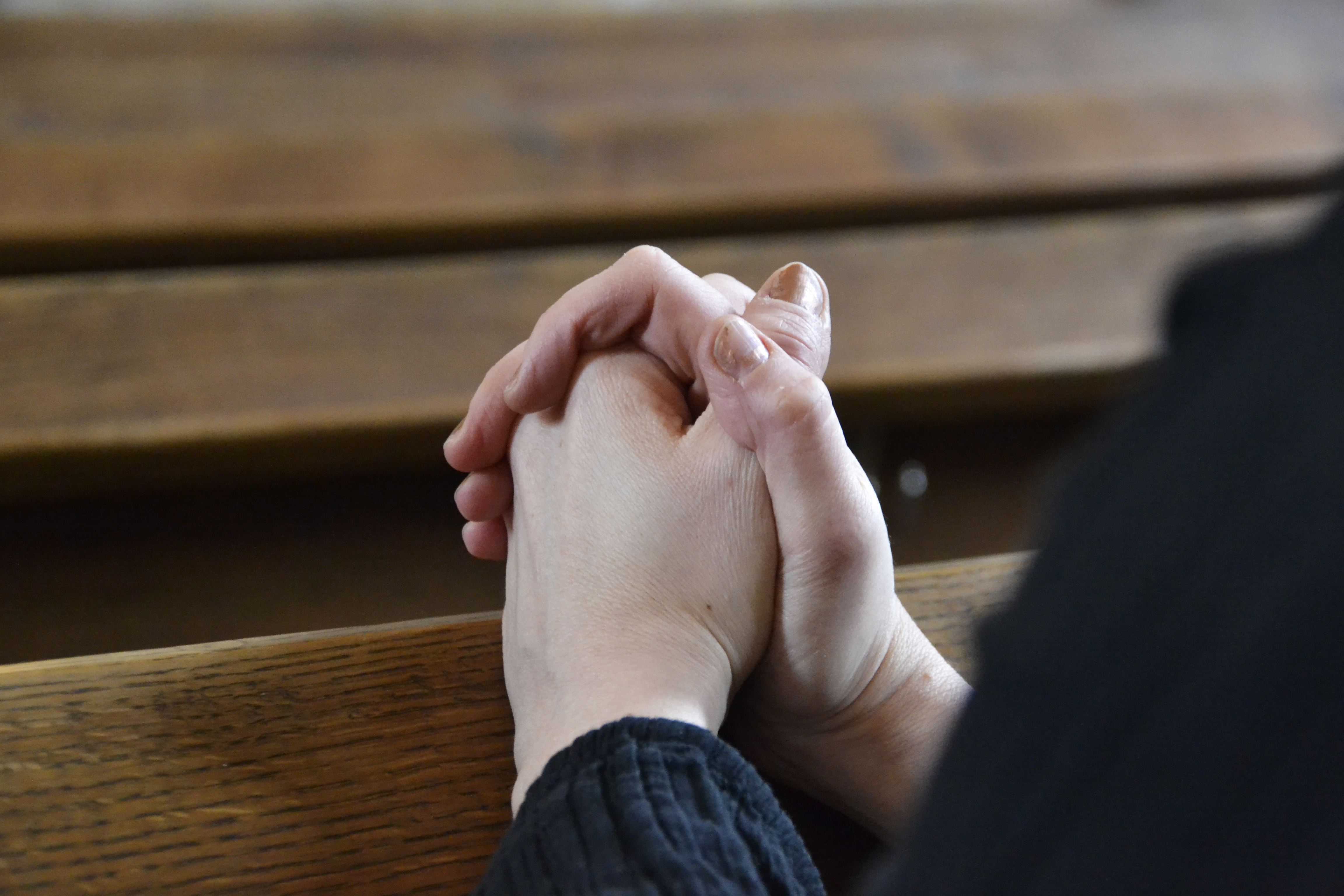 Någon sitter med knäppta händer i kyrkbänken.