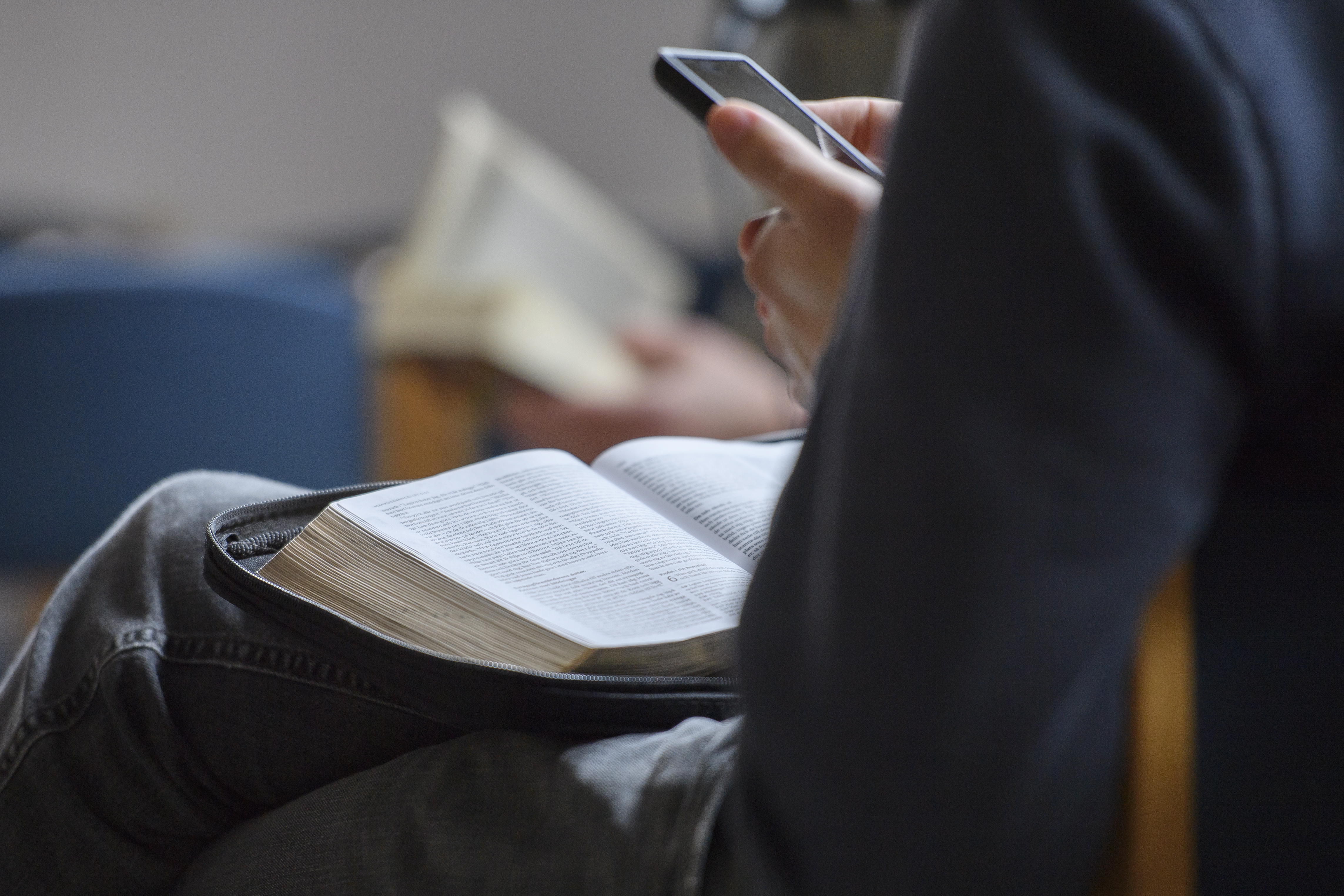 Någon sitter med en bok i knät och mobiltelefonen i handen.