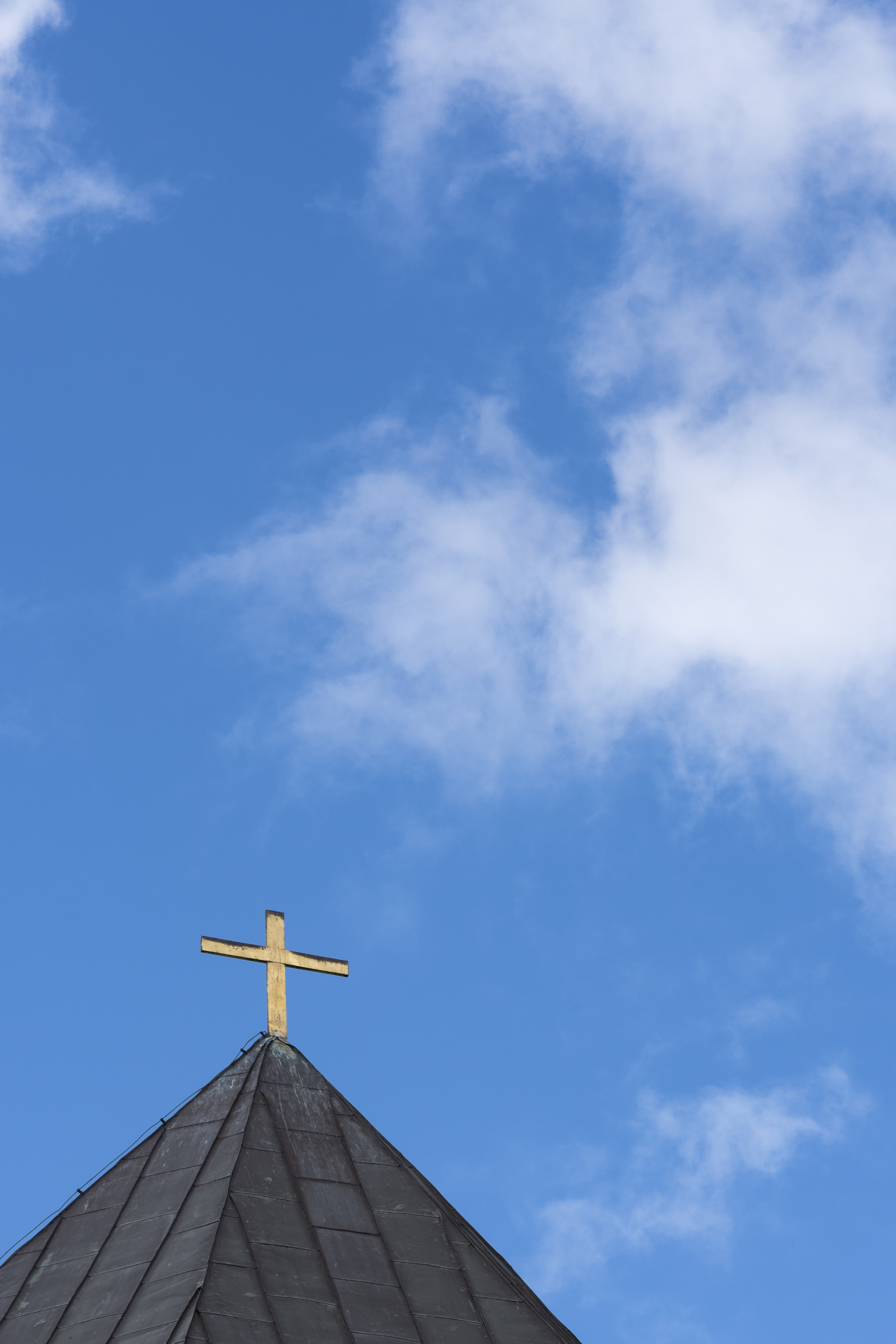 Ett kors på ett kyrktak mot blå himmel.