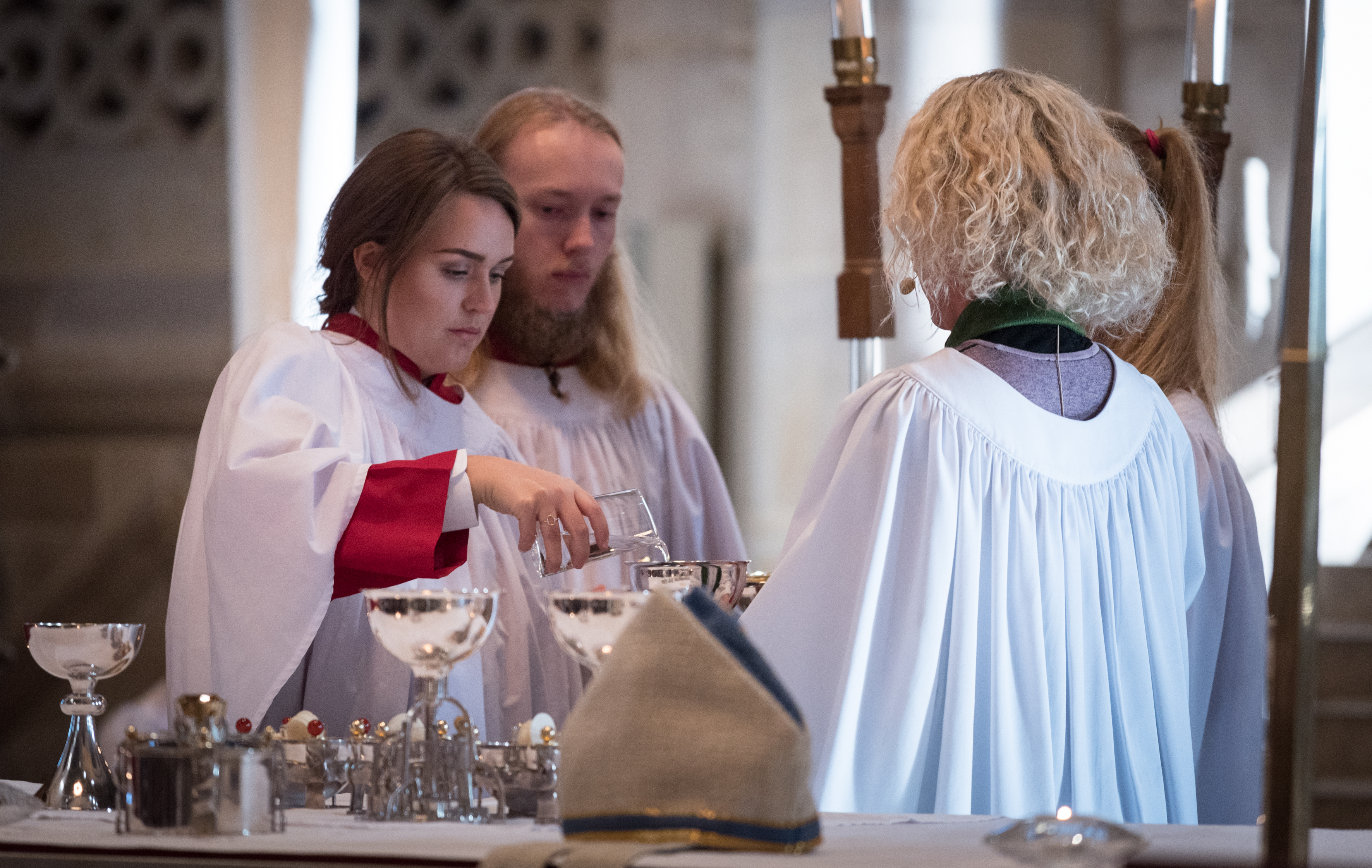 En ung kvinna i vit särk häller upp vatten i en silverpokal.