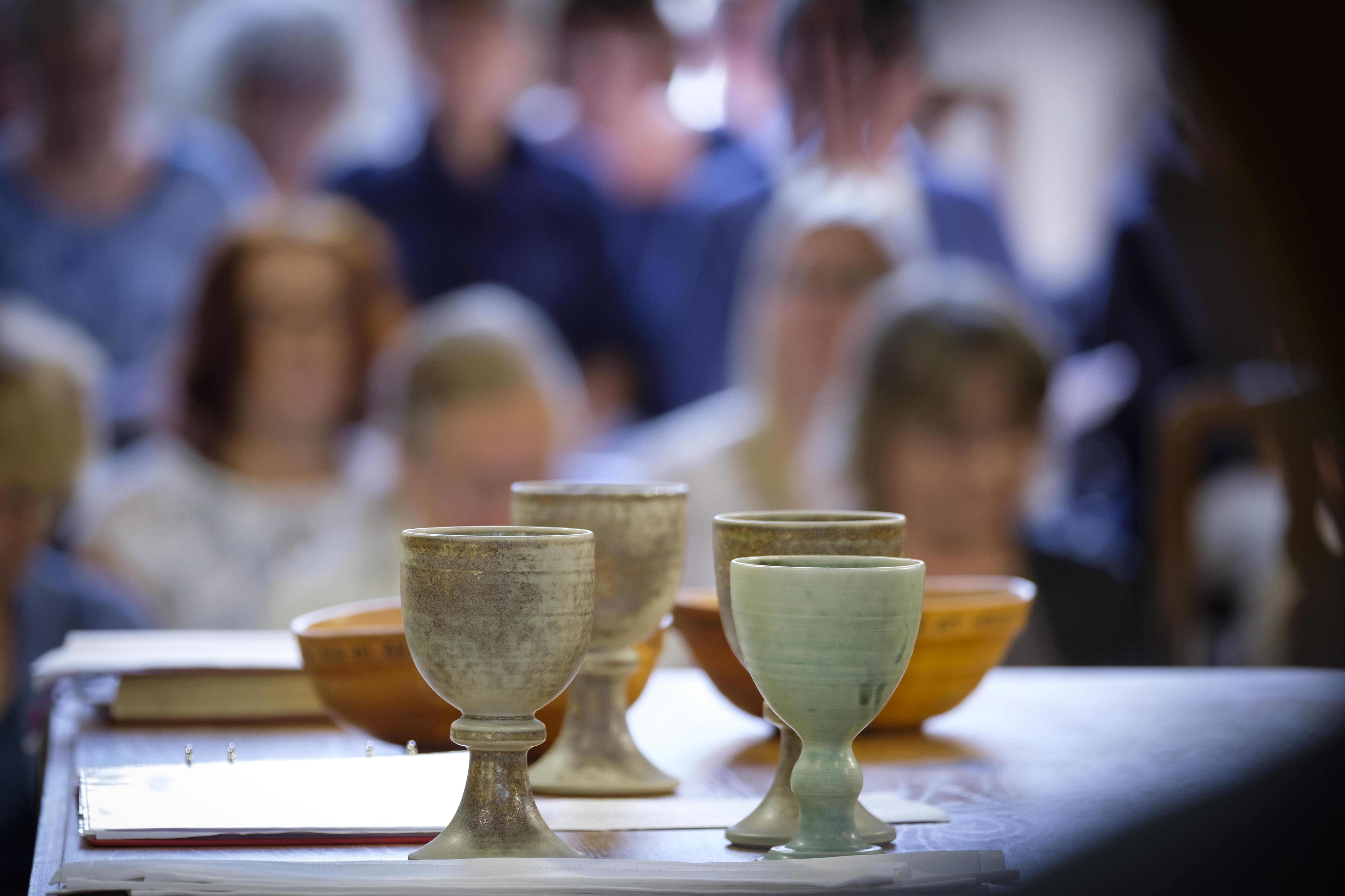 Några nattvardskalkar står på ett bord. Människor i bakgrunden.