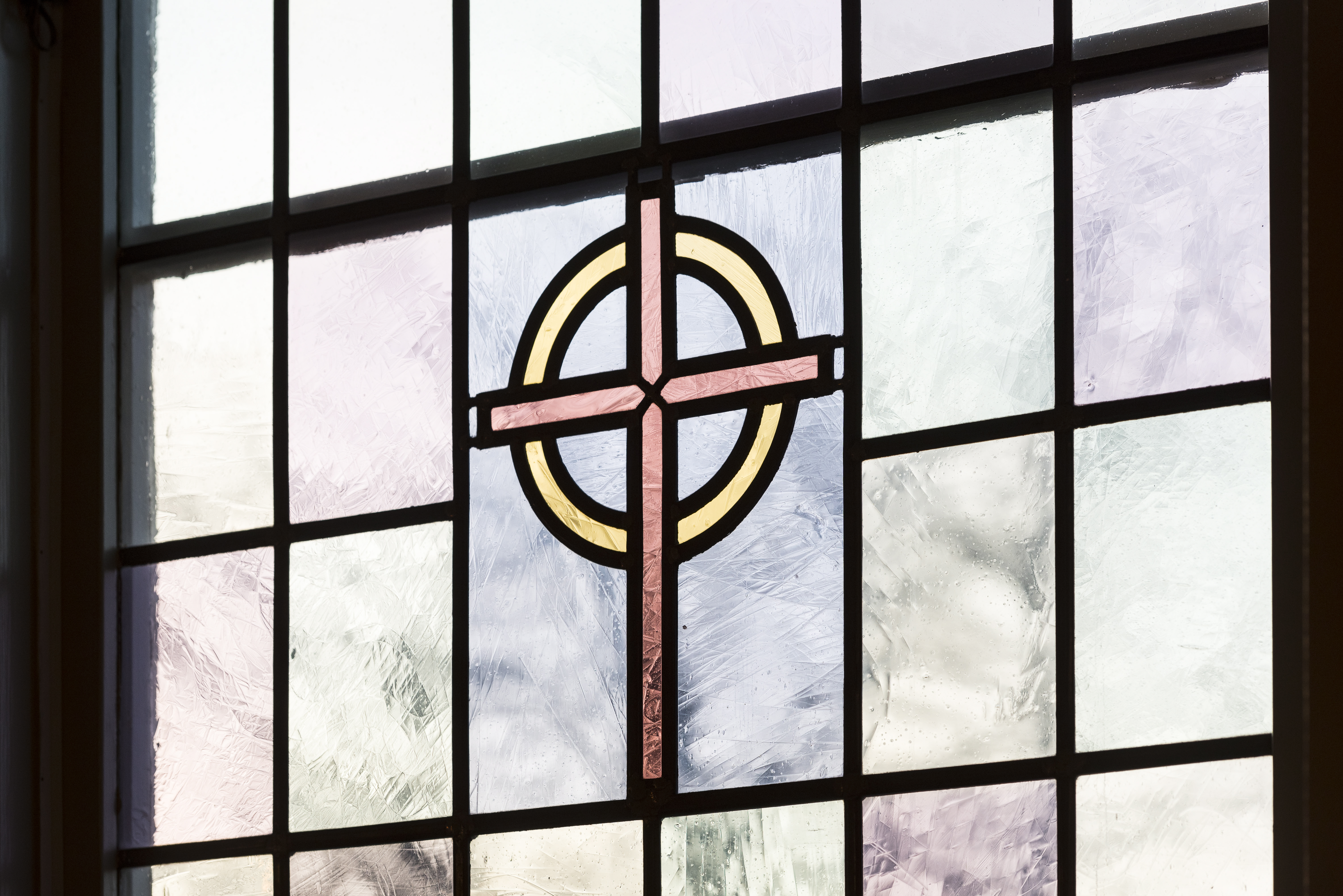 Närbild på ett färgat kyrkfönster med ett kors i mitten.