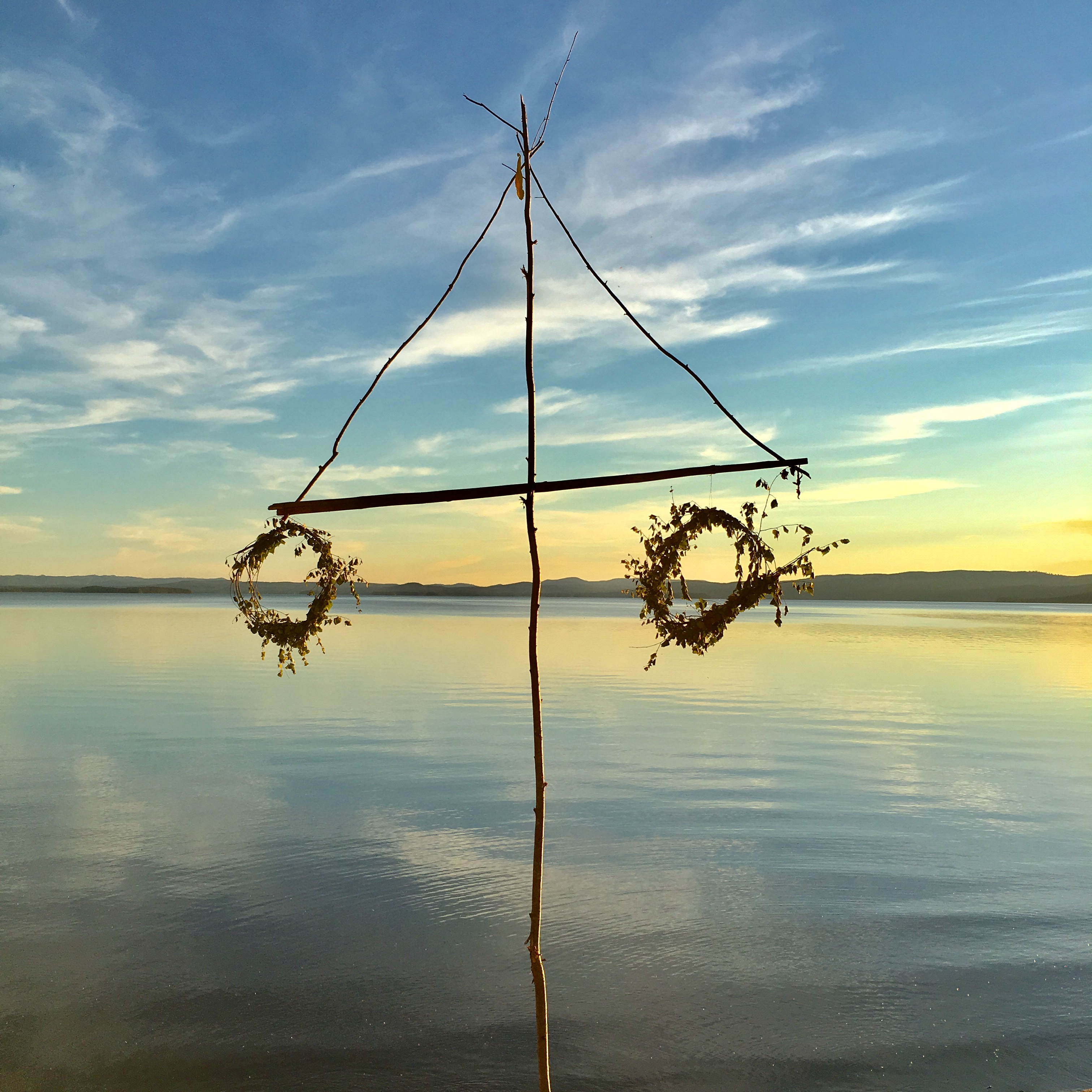 En midsommarstång med vissna kransar står vid vattnet.