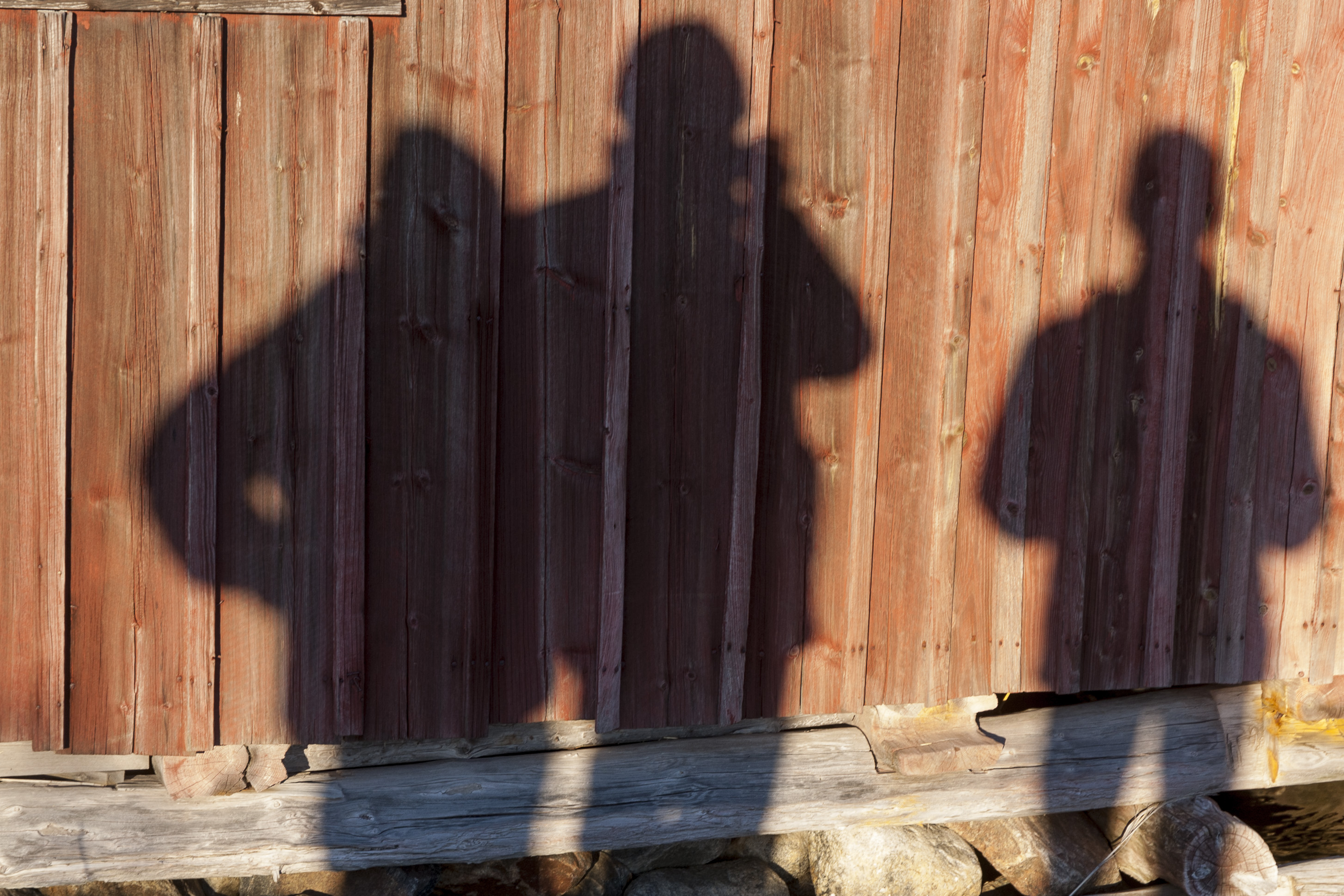 Skuggor av tre personer på väggen till en röd stuga.