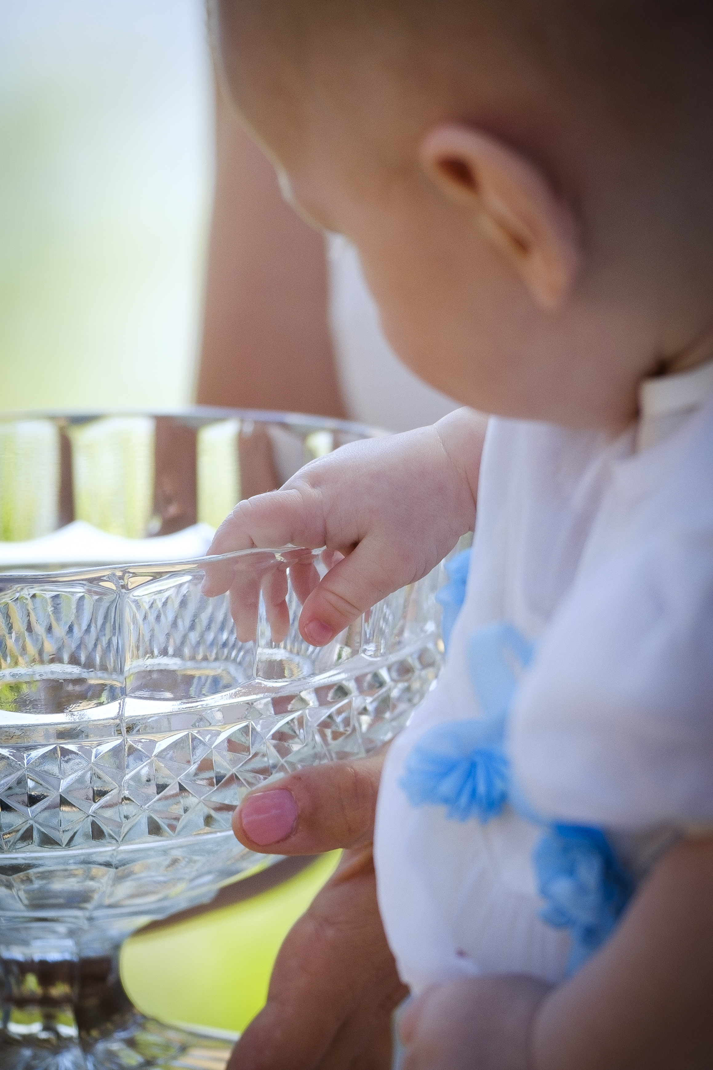 En liten bebis håller handen på kanten av en dopfunt av glas.