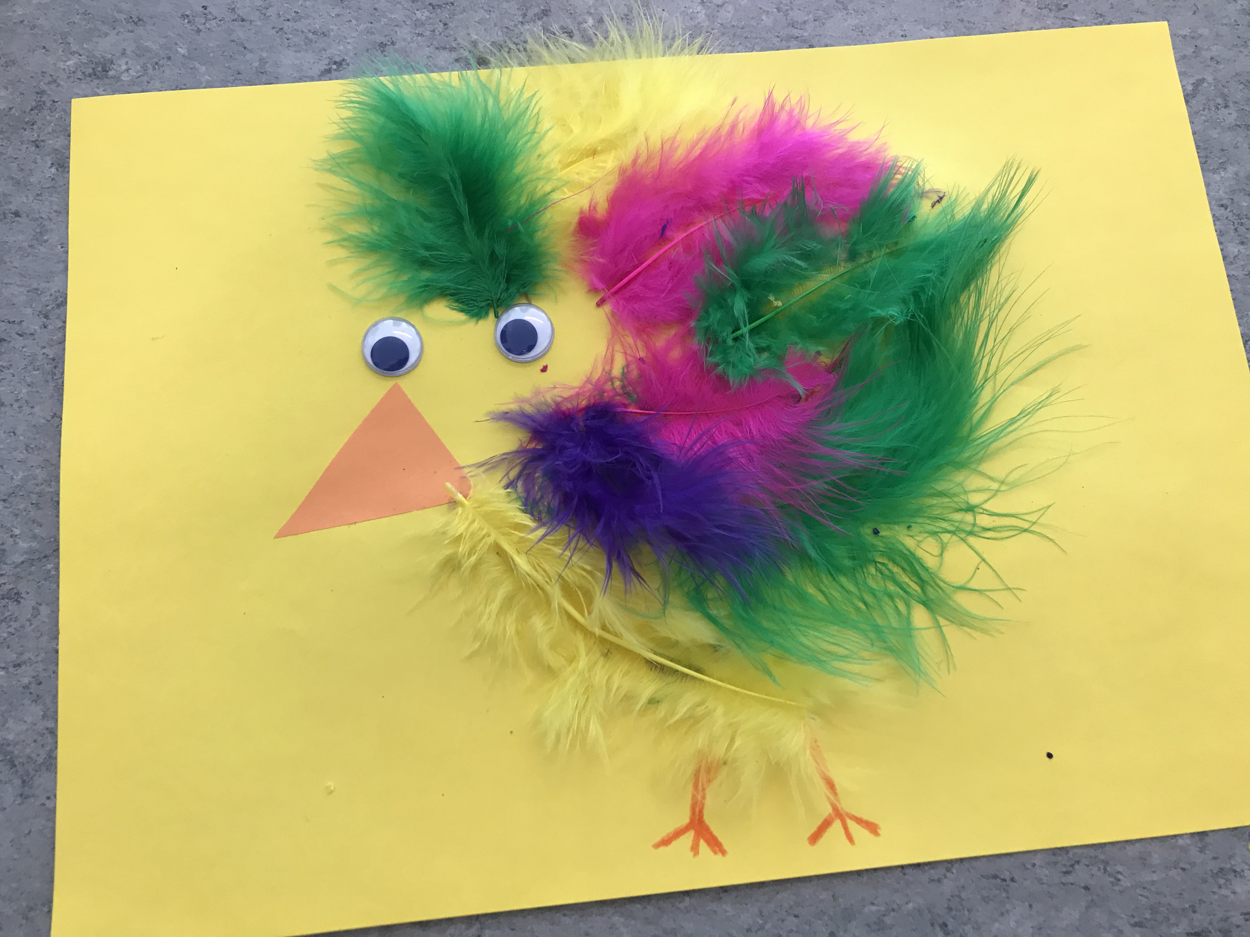 En påskkyckling på ett gult papper med färgglada fjädrar.