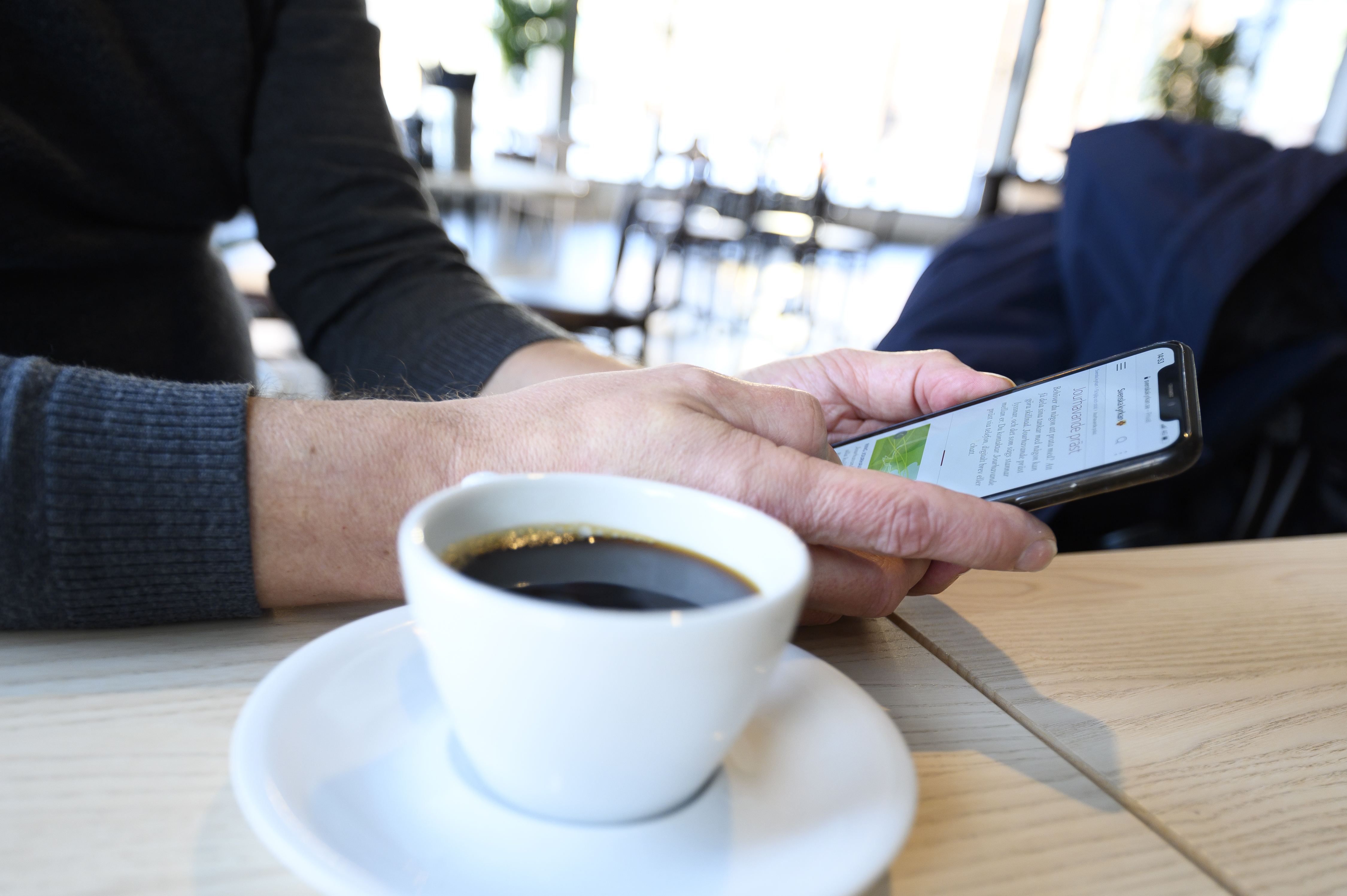 En person sitter med sin mobiltelefon och dricker kaffe.
