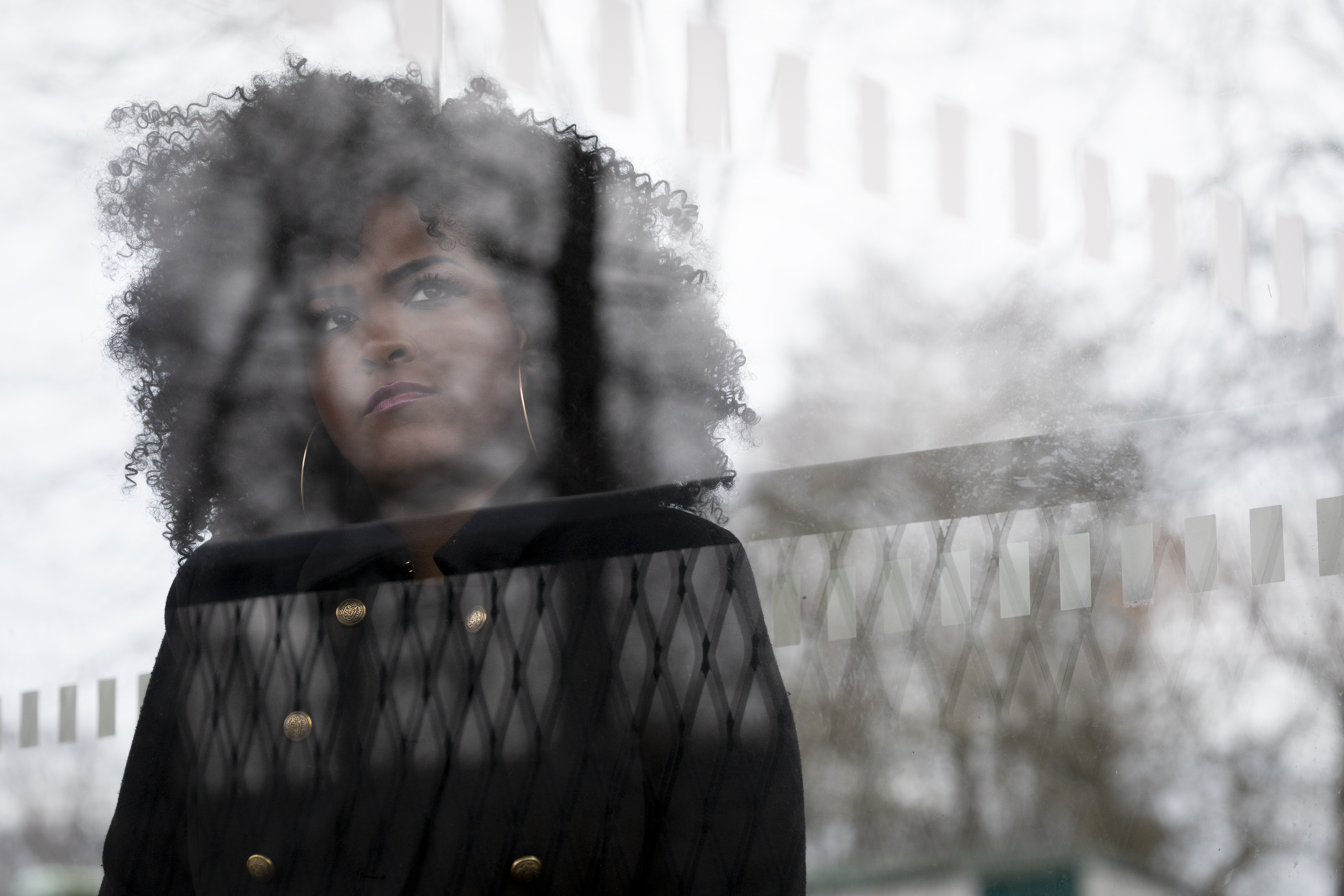 Bakom reflexerna i en busskurs glasruta syns en ung kvinna med svart lockigt hår.