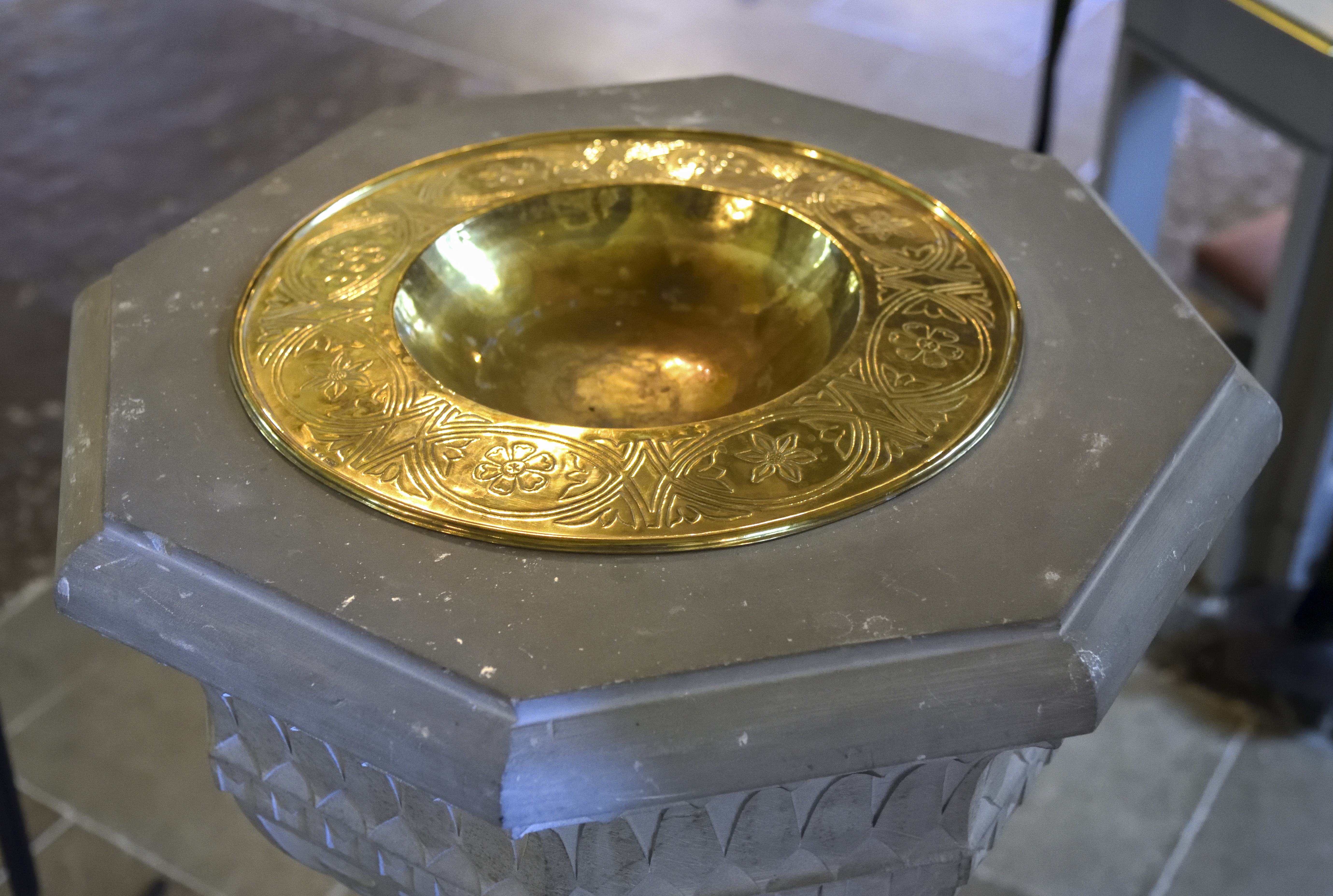 Närbild på en dopfunt i sandsten med en guldfärgad skål i metall.