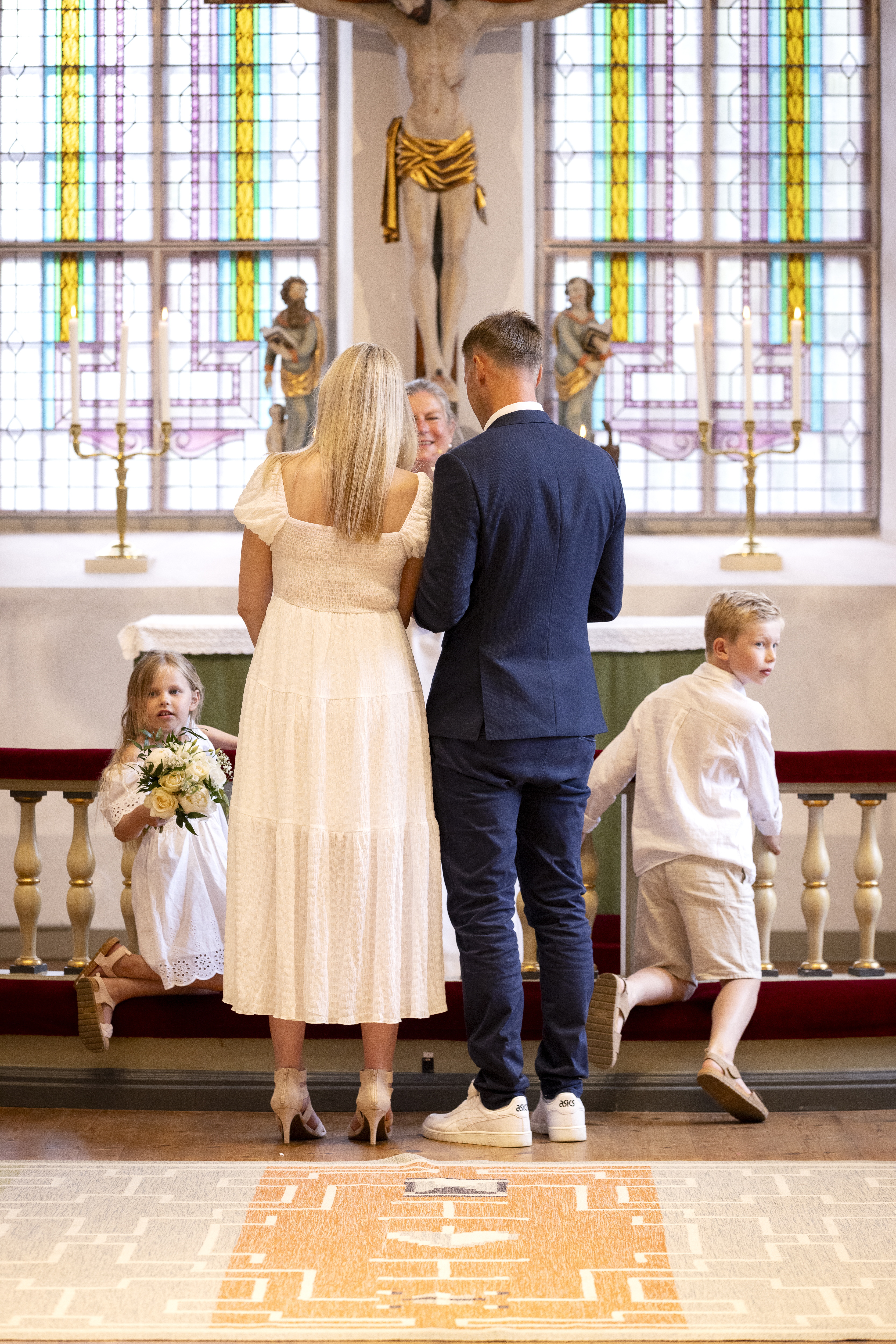 Drop-in vigsel i en kyrka. Brudparet står med ryggen mot kameran. Två barn i bakgrunden.