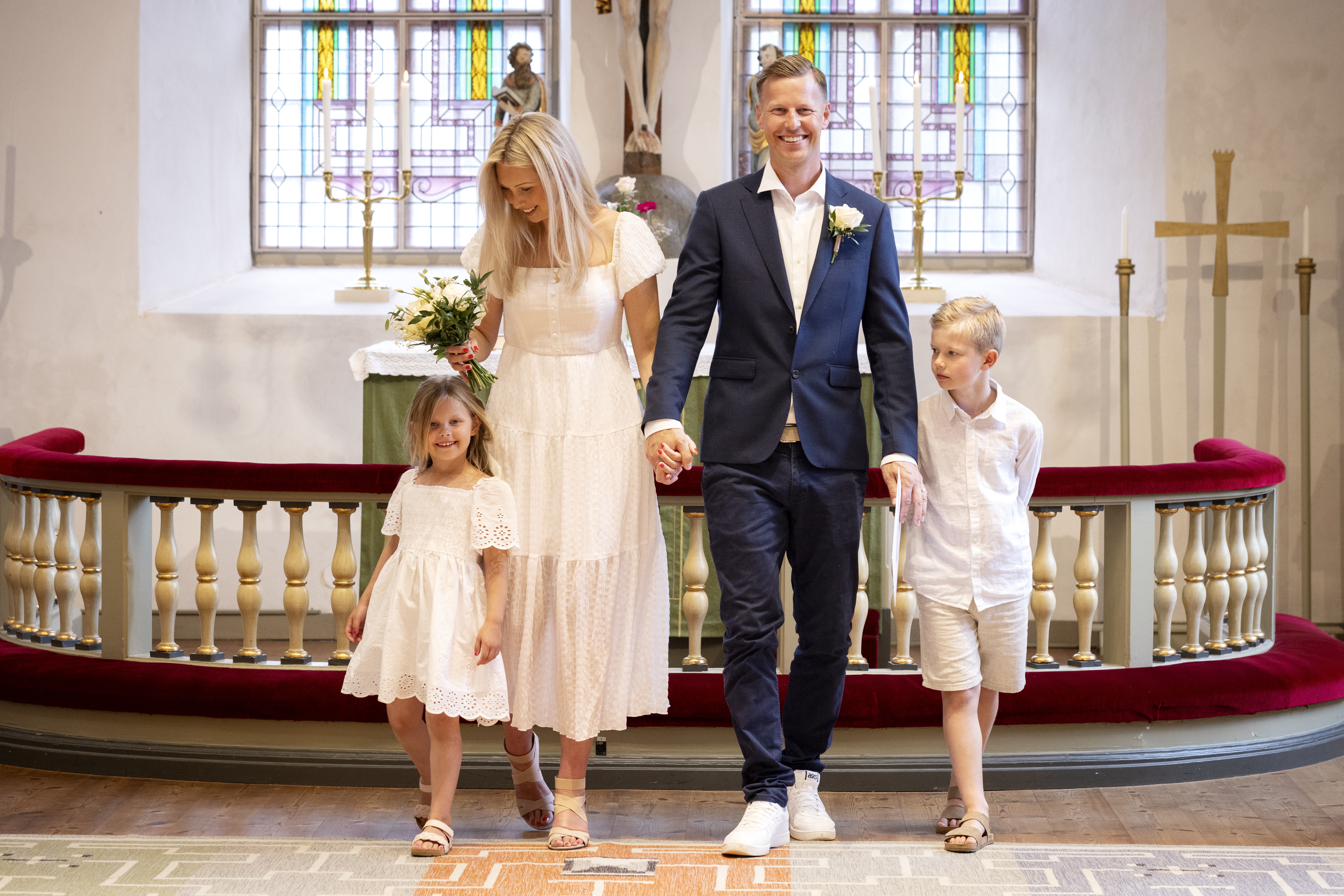 Drop-in vigsel i en kyrka. Ett brudpar står framför altarringen. Två ljusklädda barn står bredvid.