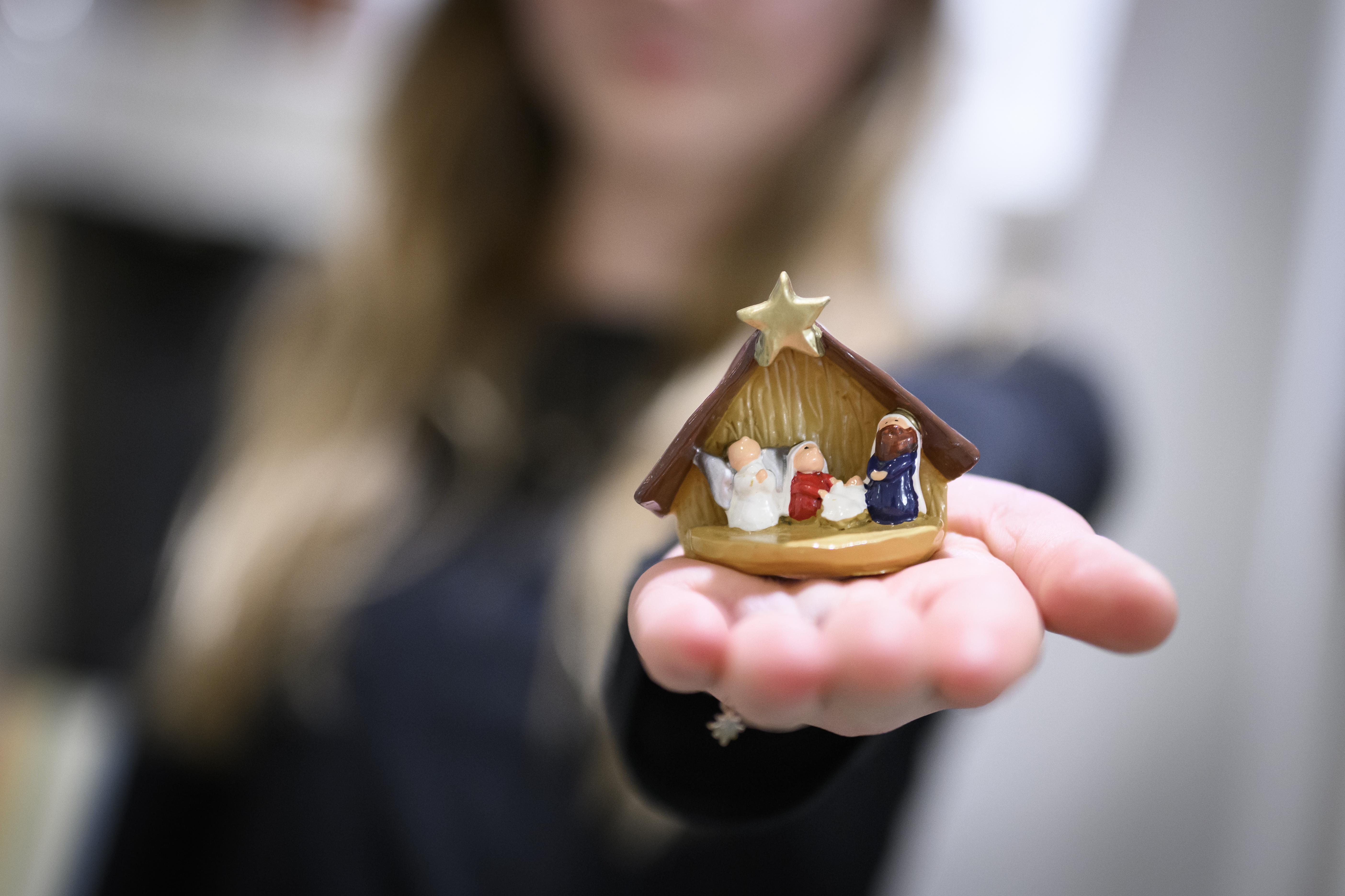 En person med utsträckt hand håller en julkrubba i miniatyr.