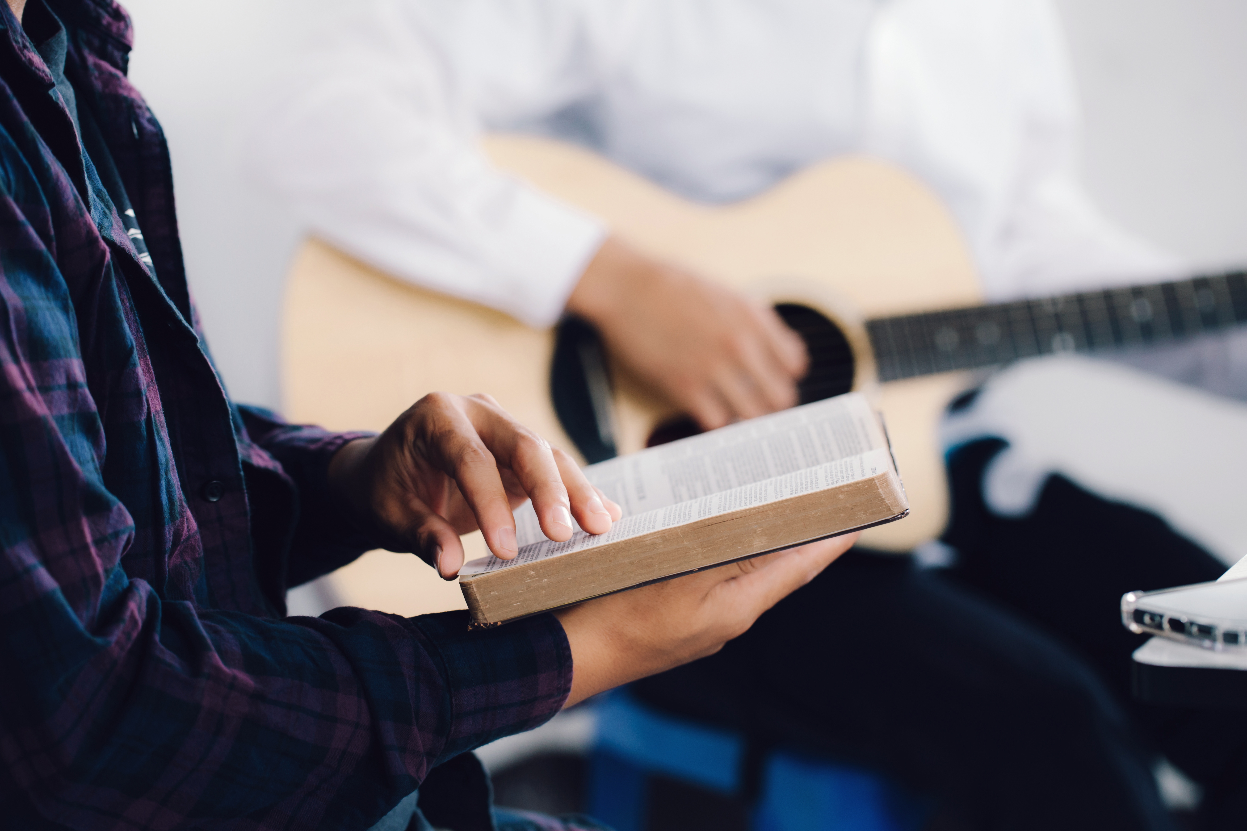 Två personer sitter bredvid varandra, en har en bibel uppslagen i sina händer, den andra spelar gitarr.