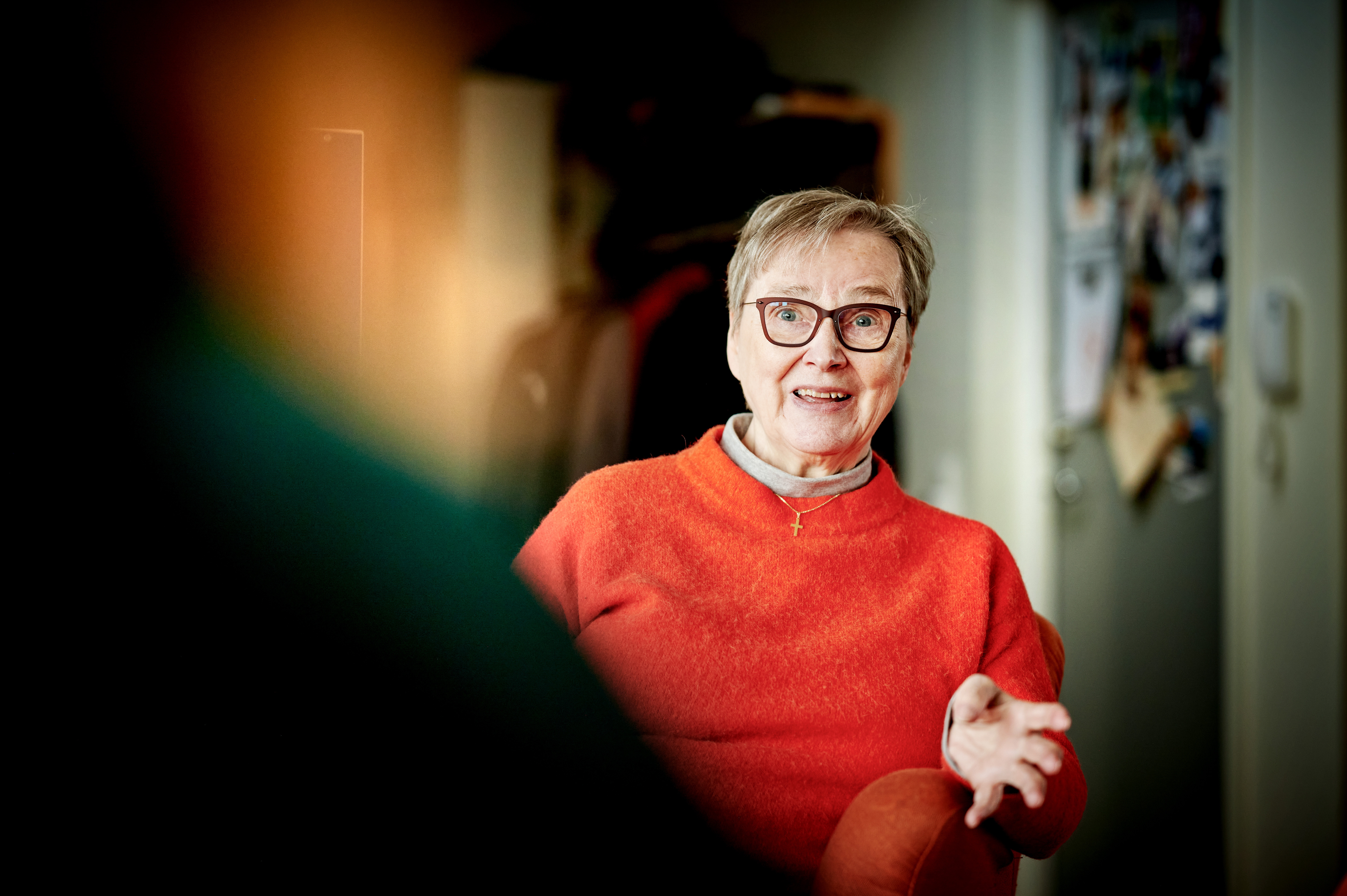 En äldre kvinna med knallorange tröja som pratar.